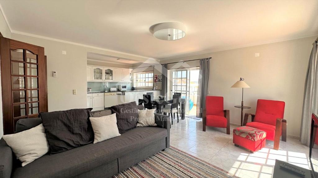 uma sala de estar com um sofá cinzento e cadeiras vermelhas em Varandas da Areia Branca em Praia da Areia Branca