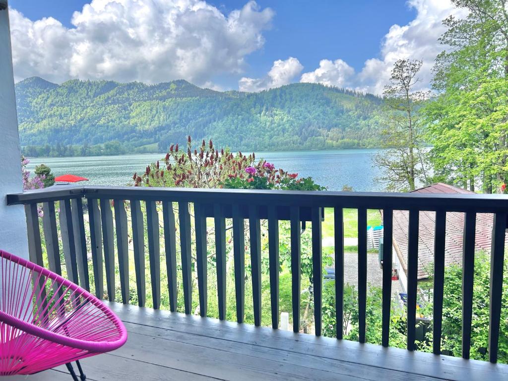 une chaise rose assise sur une terrasse avec vue sur le lac dans l'établissement Ferienwohnung Strandbad - Alpen PopArt am See, à Schliersee