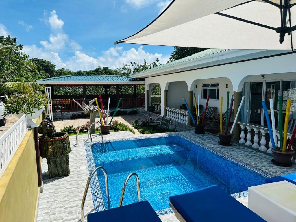 een zwembad naast een huis met een parasol bij Happy stay villa in Grand'Anse Praslin