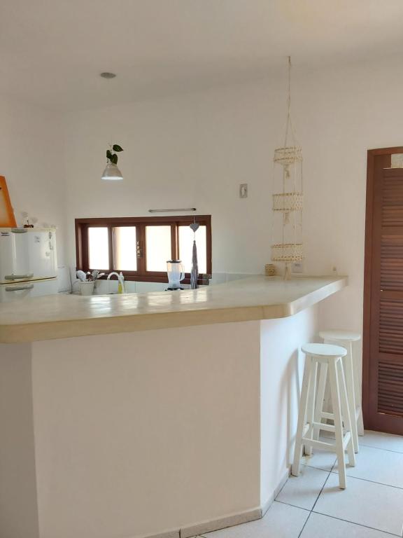 a white kitchen with a counter and a stool at Flat ideal no centro de pipa! in Pipa