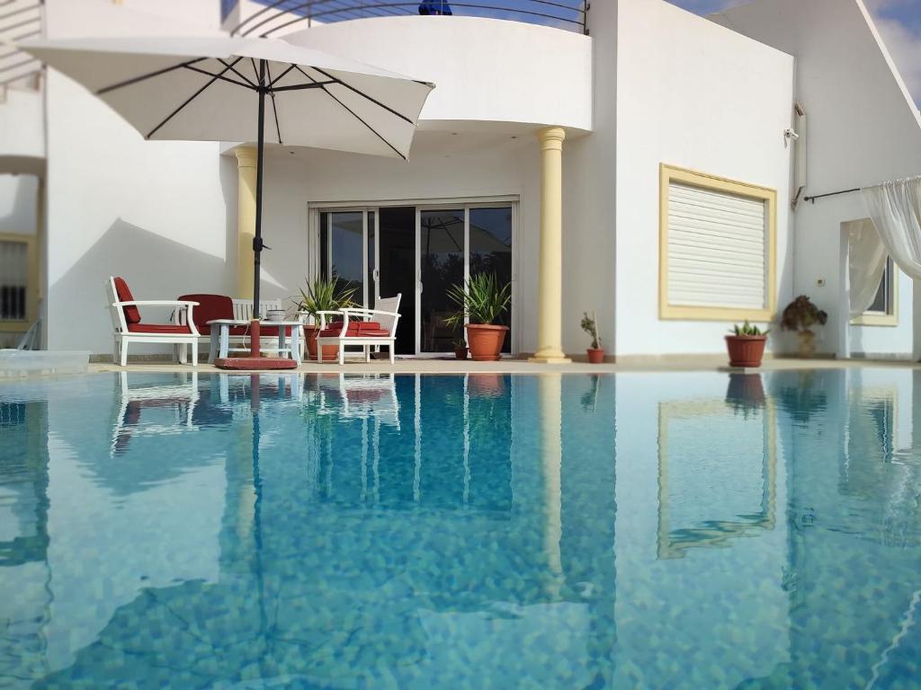 uma piscina com duas cadeiras e um guarda-sol em Chambres d'hôtes Conviviales avec piscine privée Chambre Namasté et Chambre Rose des Sables em Djerba