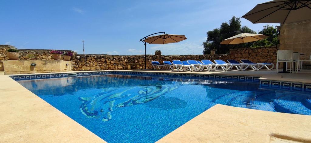 a swimming pool with chairs and umbrellas at Warda Accommodation in Xewkija