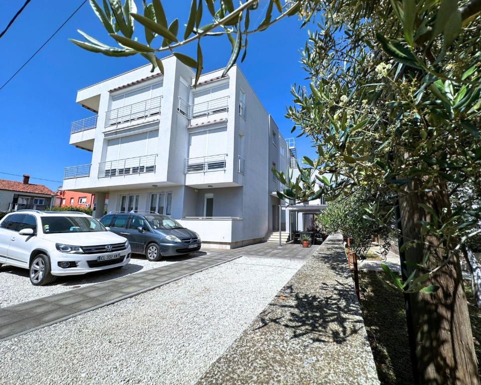 ein weißes Gebäude mit Autos auf einem Parkplatz in der Unterkunft The Martinez Holiday House - Zadar in Zadar