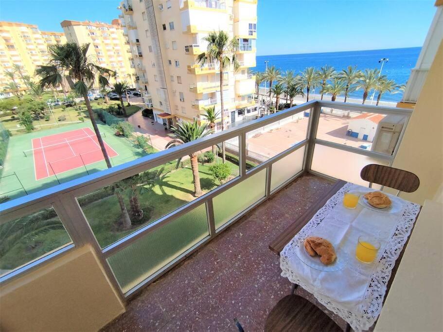 un balcone con tavolo e 2 bevande e un campo da tennis di Beachfront apartment ALG-Costa a Algarrobo-Costa