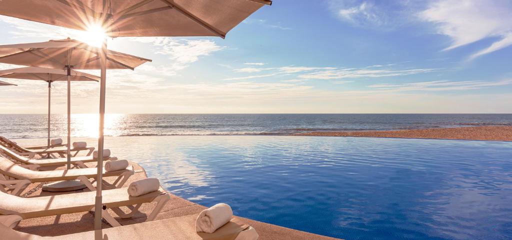 una piscina con sillas, una sombrilla y el océano en Park Royal Beach Mazatlán, en Mazatlán
