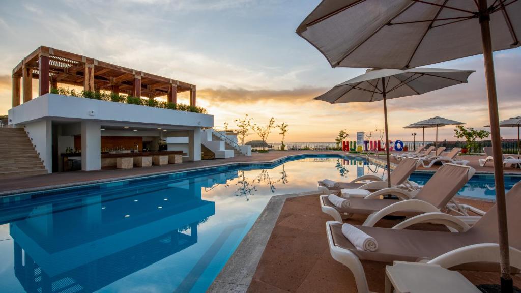 uma piscina com cadeiras e guarda-sóis em frente a um hotel em Park Royal Beach Huatulco - All Inclusive em Santa Cruz, Huatulco