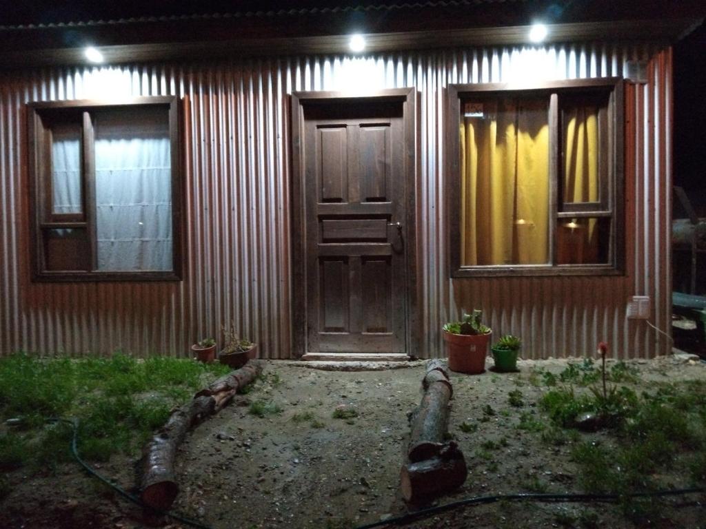 une maison avec une porte en bois et des fenêtres la nuit dans l'établissement Cabaña La Guanaca, à Comandante Luis Piedrabuena