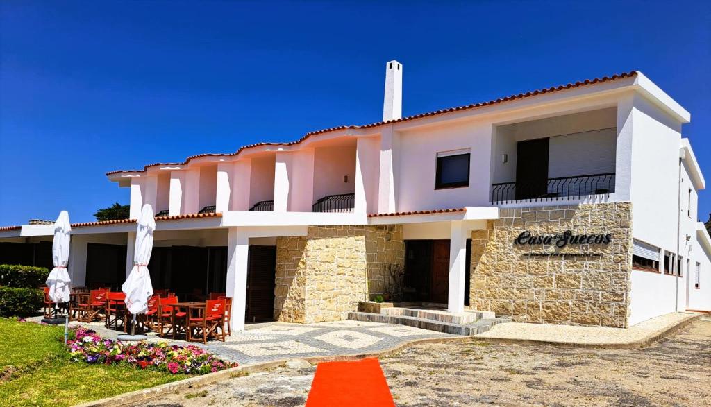 un grand bâtiment blanc avec des chaises et des parasols dans l'établissement Boutique Inn & Restaurant - Casa dos Suécos, à Figueira da Foz