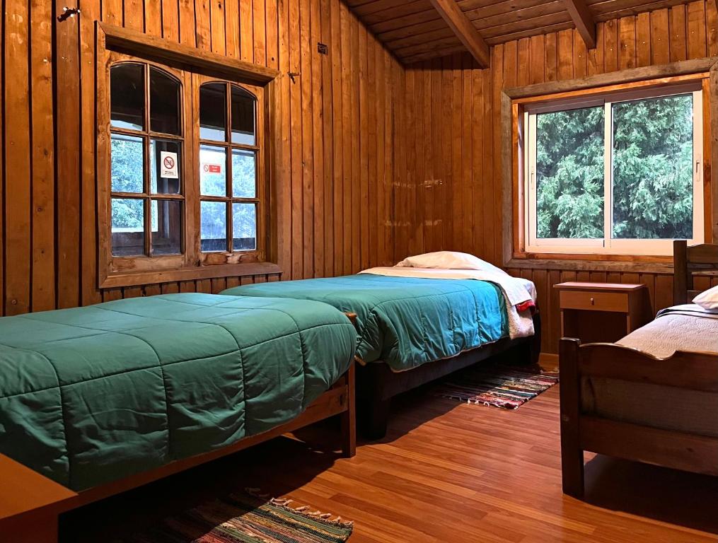 two beds in a room with wooden walls and windows at Hostel del Valle in Recinto