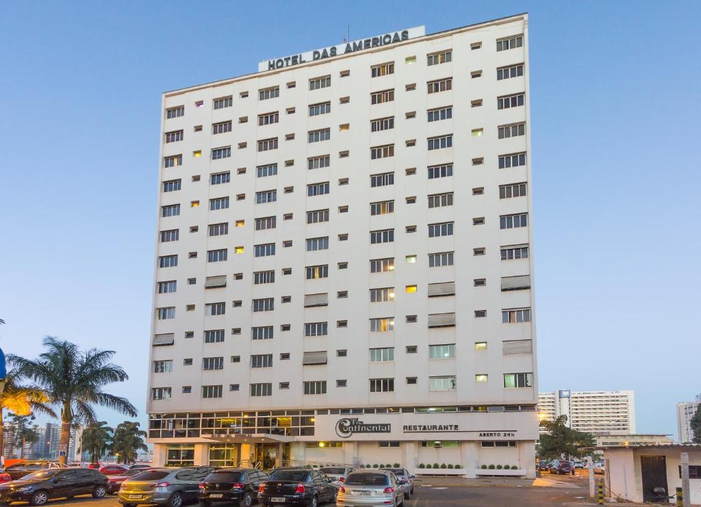 un grande edificio bianco con auto parcheggiate in un parcheggio di América Bittar Hotel a Brasilia