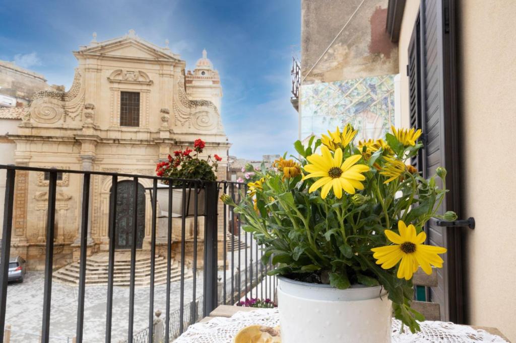 un vase de fleurs jaunes sur un balcon avec un bâtiment dans l'établissement Bellavista apartment, à Caltagirone