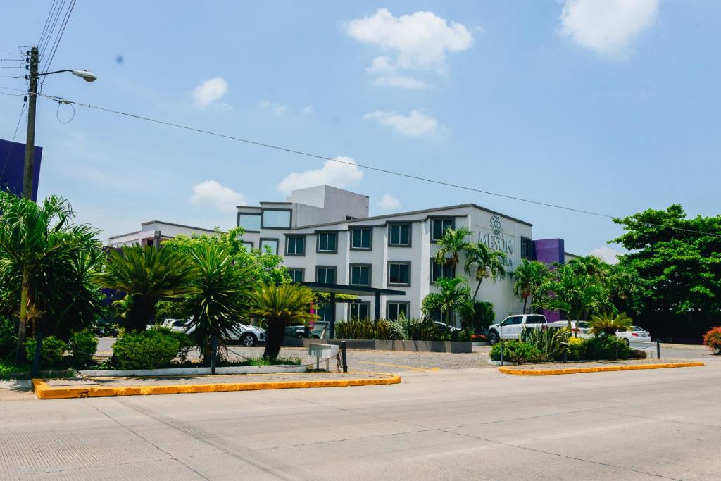 a white building with palm trees in front of a street at Hotel Mesón de la Chinantla in San Juan Bautista Tuxtepec