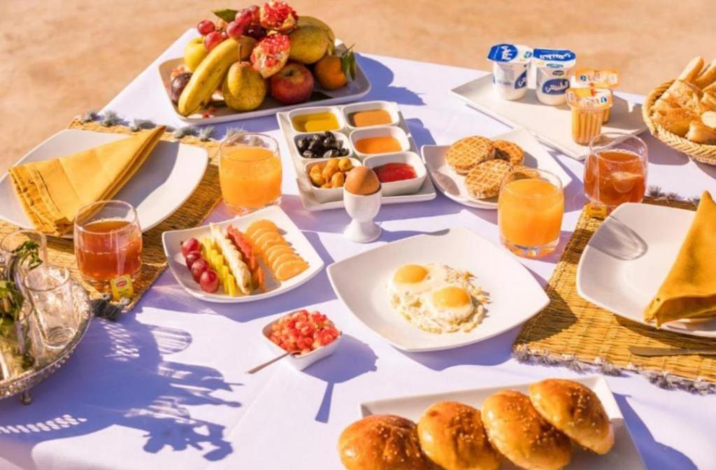 Una mesa cubierta con platos de desayuno y jugo de naranja. en Original Luxury Camp, en Merzouga