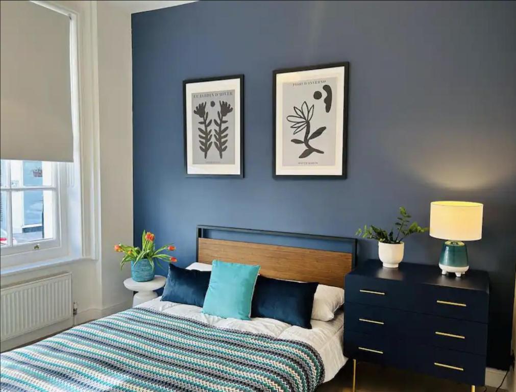 a bedroom with a blue wall with a bed and a dresser at Gorgeous split level Belsize Park Apartment in London