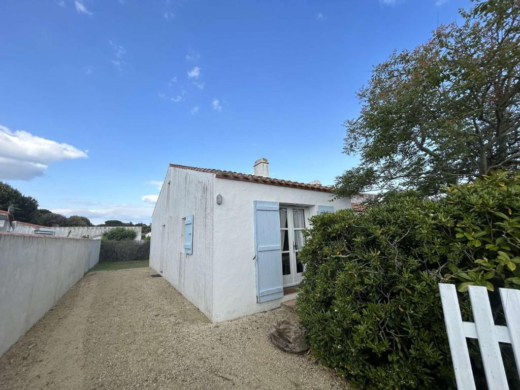 une maison blanche avec une fenêtre bleue et une clôture dans l'établissement Maison cosy avec mezzanine, proche plage et commerces, terrasse tranquille - Noirmoutier-en-l'Île - FR-1-224B-606, à Noirmoutier-en-l'lle