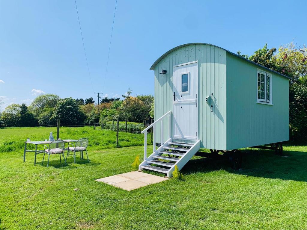 a small green shed with a table and a table at Bells Meadow Shepherds Hut in Kings Lynn