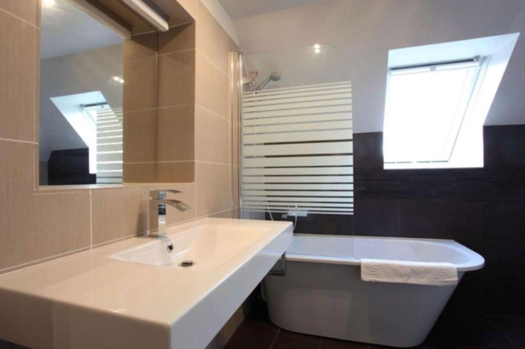 een badkamer met een wastafel, een bad en een raam bij Rheinländer Seehotel in Leverkusen