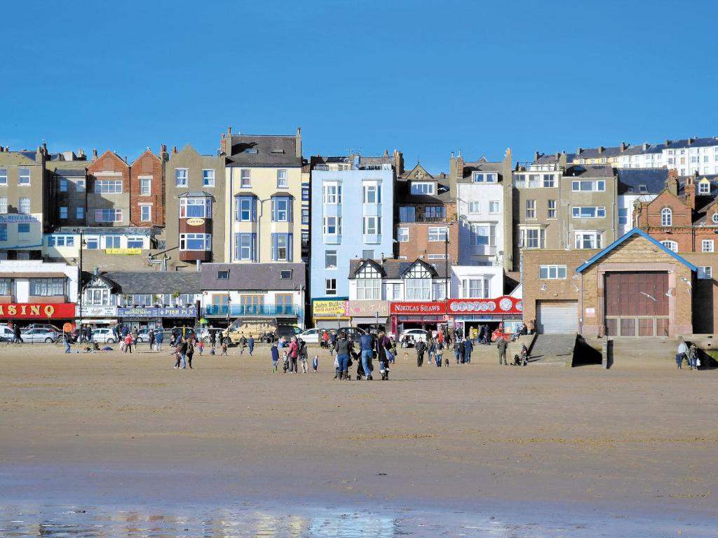 a group of people walking on a beach with buildings at Sea Blue Cottage in Scarborough