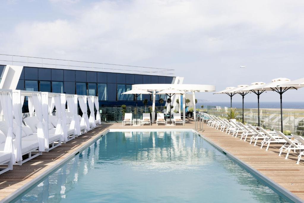 a swimming pool with white chairs and umbrellas at Sheraton Nice Airport in Nice