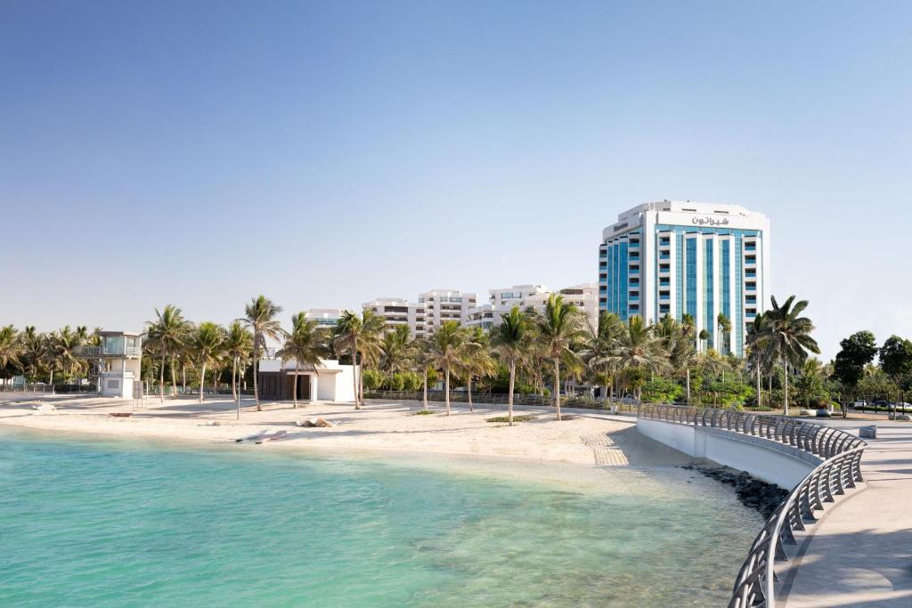 فندق شيراتون جدة في جدة: شاطئ فيه نخيل ومبنى طويل