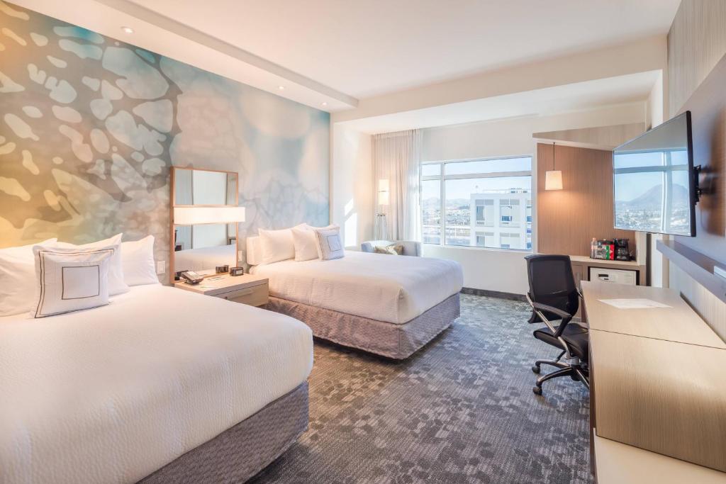 チワワにあるCourtyard by Marriott Chihuahuaのベッド2台とデスクが備わるホテルルームです。