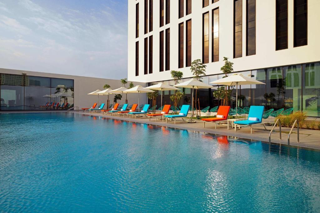 a swimming pool with chairs and umbrellas in front of a building at Aloft Me'aisam, Dubai in Dubai