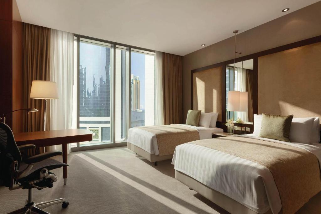 JW Marriott Marquis City Center Doha في الدوحة: غرفة فندقية بسريرين ومكتب ونافذة