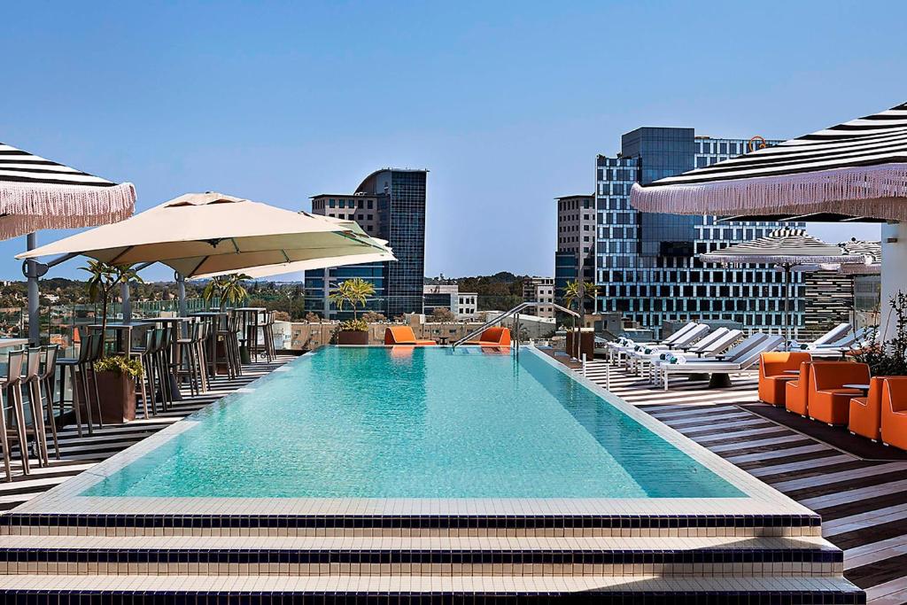 a swimming pool with chairs and umbrellas on a building at Publica Isrotel, Autograph Collection in Herzliya