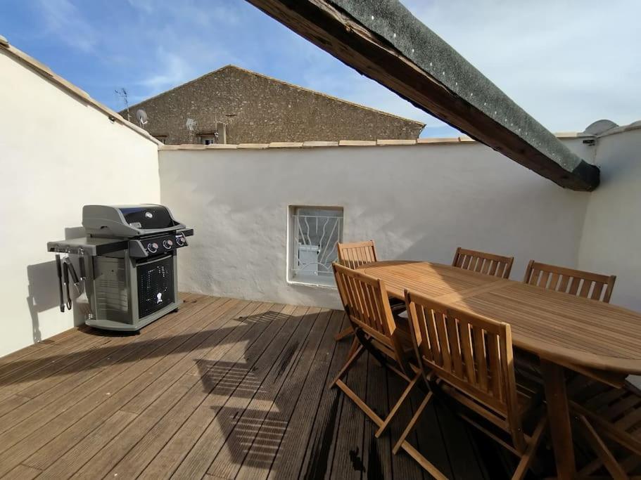 une terrasse en bois avec une table en bois et un grill dans l'établissement Maison de village avec terrasse proche plages, à Lespignan