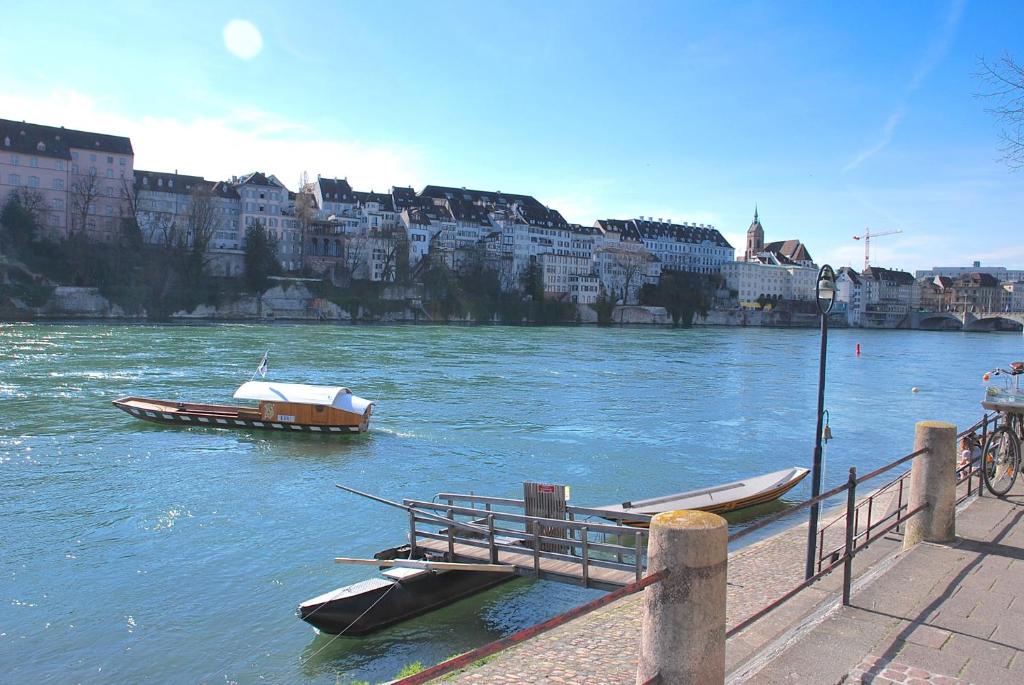 due barche sono ormeggiate su un fiume con edifici di RIVERSIDE - APARTMENTS BASEL deluxe a Basilea