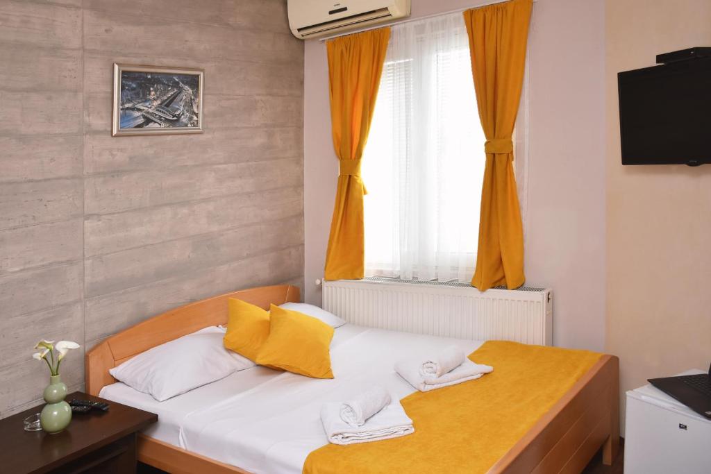 1 dormitorio con 1 cama con cortinas amarillas y ventana en Guest House Villa Mir, en Kragujevac