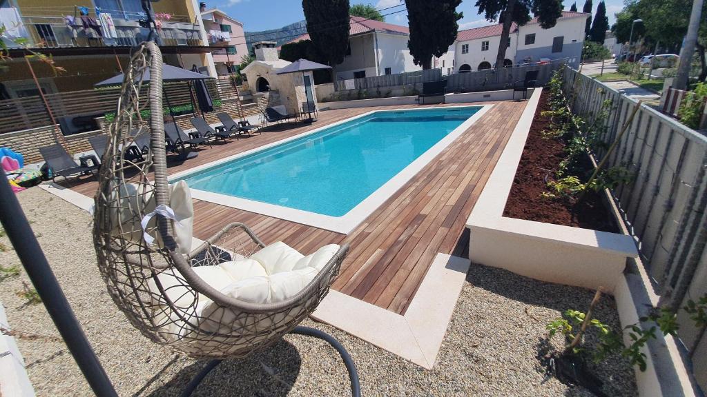 a swimming pool with a chair and a hammock next to a house at Apartments Meštrović in Kaštela