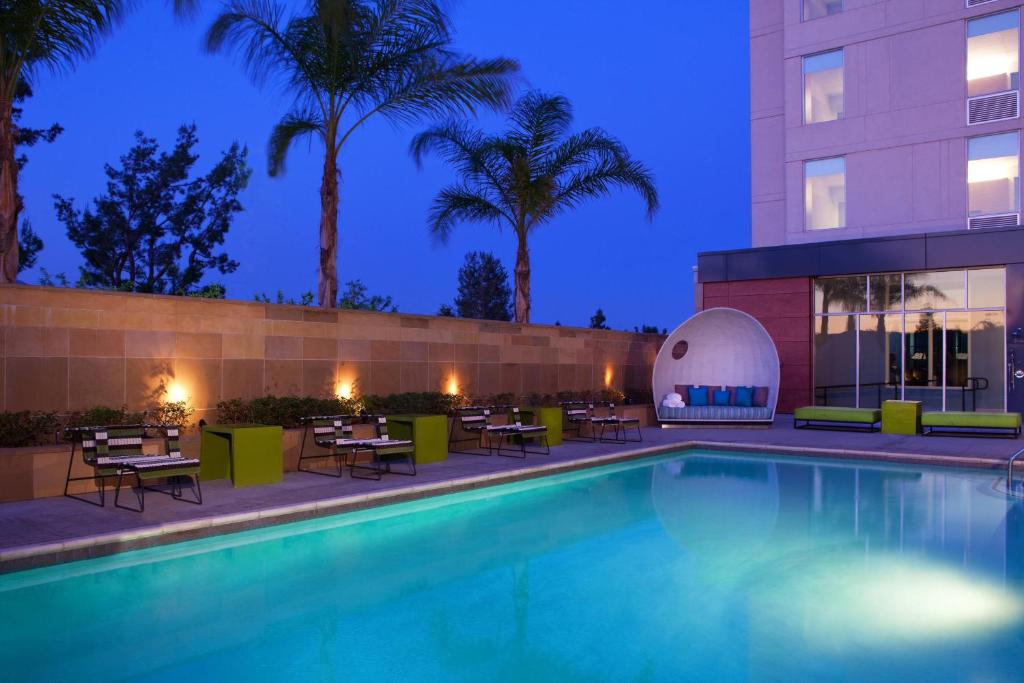 a swimming pool with tables and chairs next to a building at Aloft Ontario-Rancho Cucamonga in Rancho Cucamonga