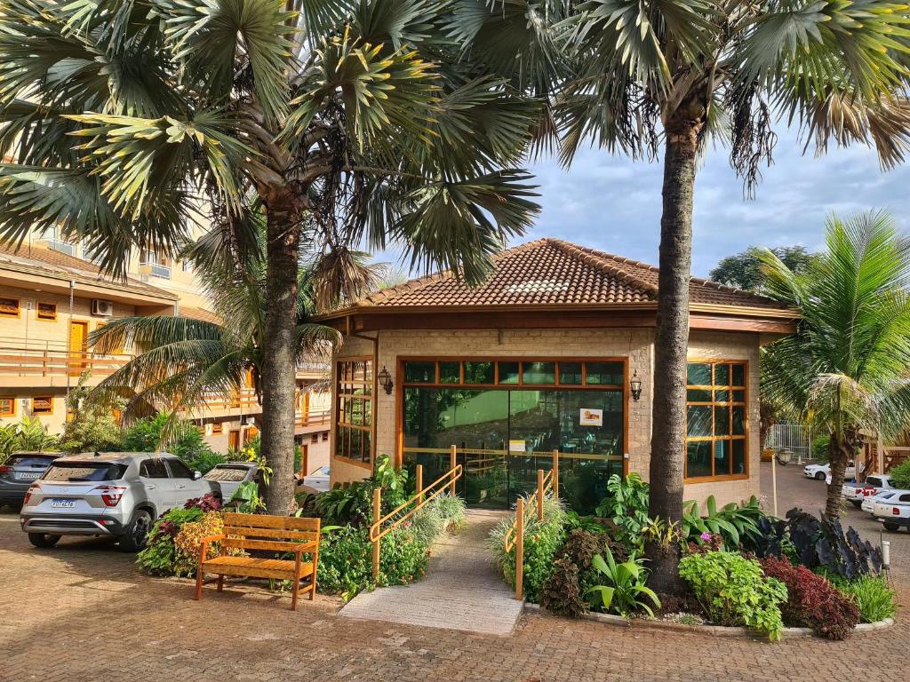 a building with palm trees and a bench in front of it at Hotel Pousada Santa Rita in Ribeirão Preto