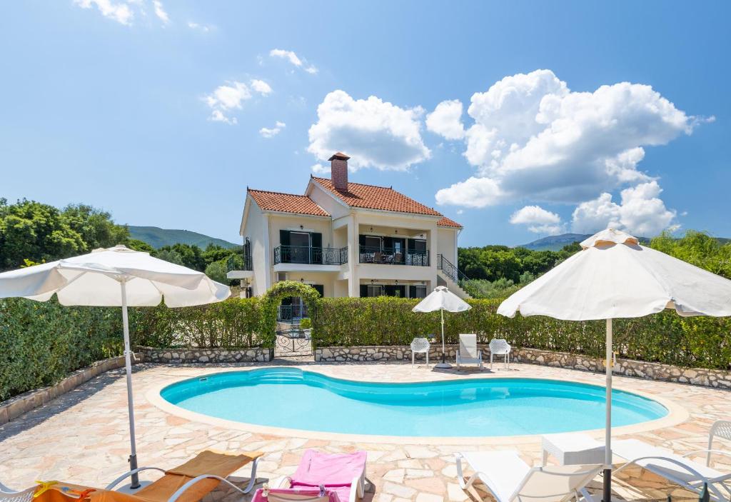 a pool with chairs and umbrellas in front of a house at Arte villa Margarita apartment in Karavomylos