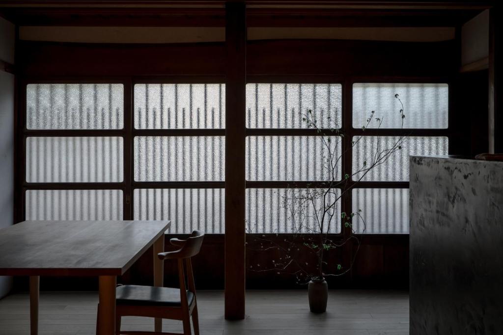 Zimmer mit 3 Fenstern, einem Tisch und Stühlen in der Unterkunft Shiroyamakan in Shirakawa-gō