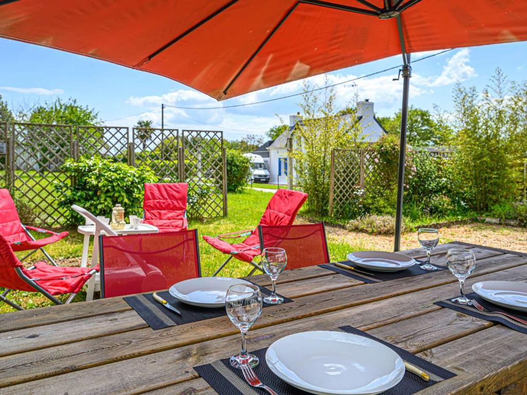 een houten tafel met rode stoelen en een parasol bij Villa Landaul, 4 pièces, 6 personnes - FR-1-479-152 in Landaul