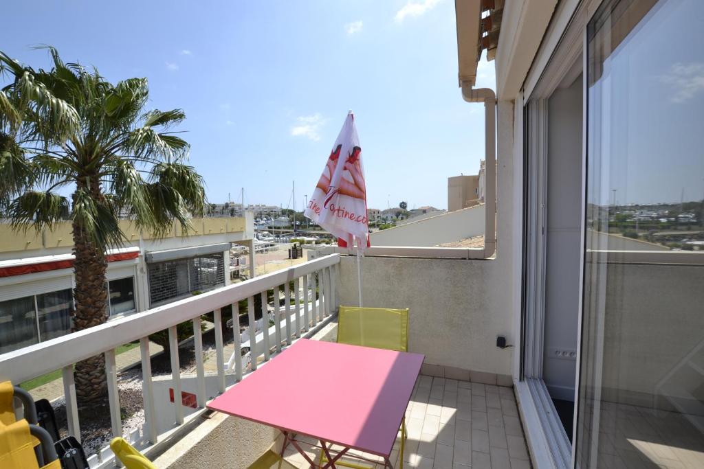une table et des chaises roses sur un balcon avec un palmier dans l'établissement Studio Naturiste ALBATROS Port Soleil 544, au Cap d'Agde