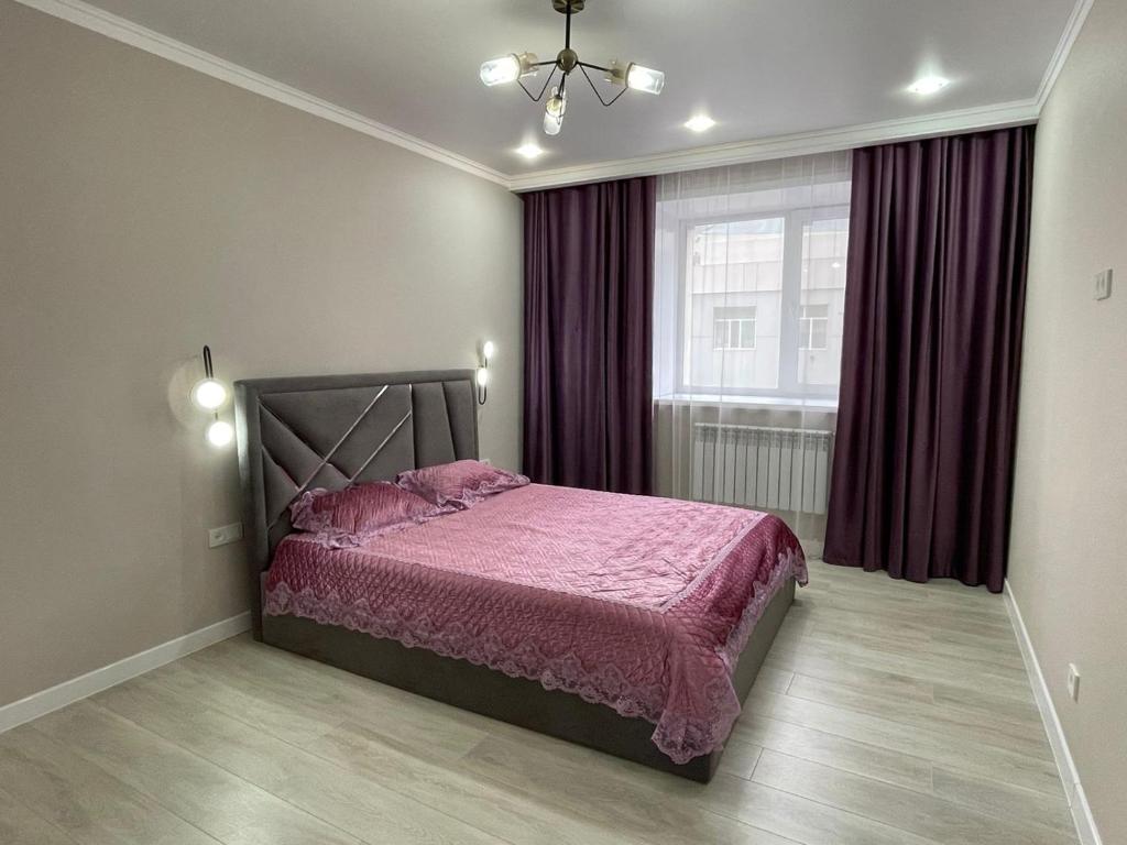 1 dormitorio con 1 cama con edredón rosa y ventana en Ауезова 189б ЖК в центре en Kokshetau