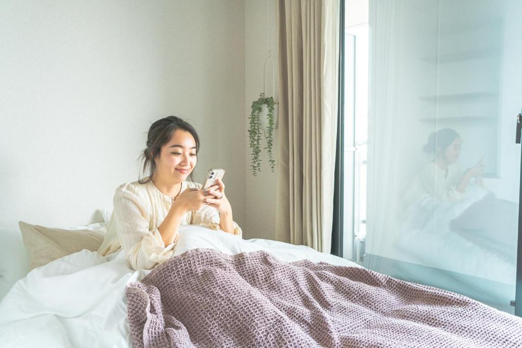 a woman sitting in bed looking at her cell phone at i-rent京急蒲田 in Tokyo