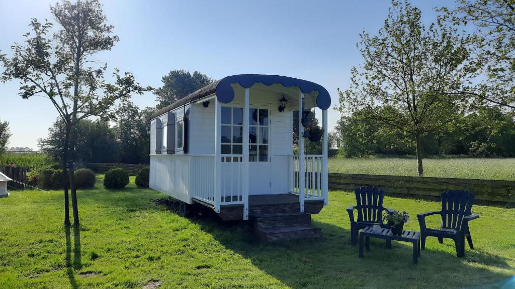 a tiny house in a yard with two chairs at Pipowagen 't Strunerke in Augustinusga