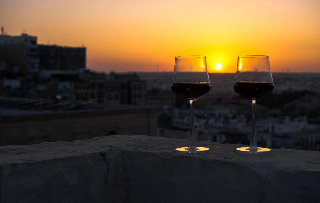 due bicchieri di vino seduti su un cornicione con il tramonto di Mulberry Suites a La Valletta