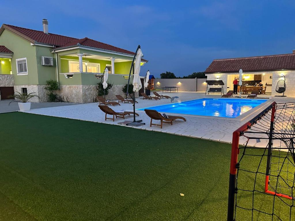 a swimming pool with chairs and a house at IDILA in Sveti Filip i Jakov