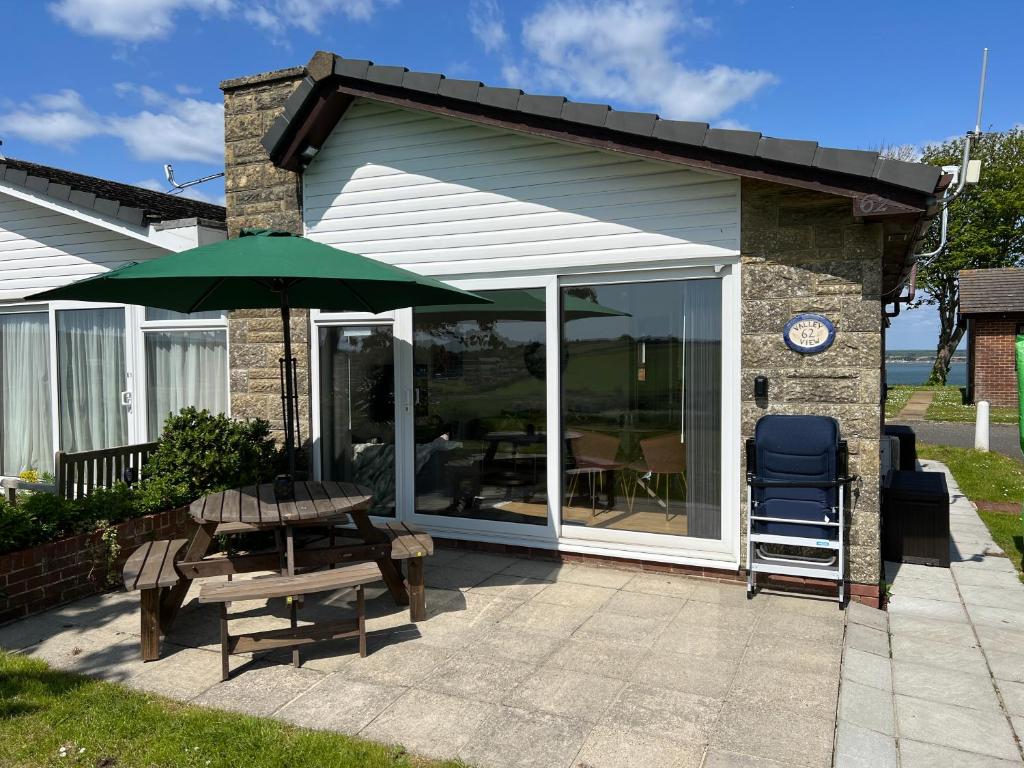 eine Terrasse mit einem Tisch und einem grünen Sonnenschirm in der Unterkunft VALLEY VIEW self-catering coastal bungalow in rural West Wight in Freshwater