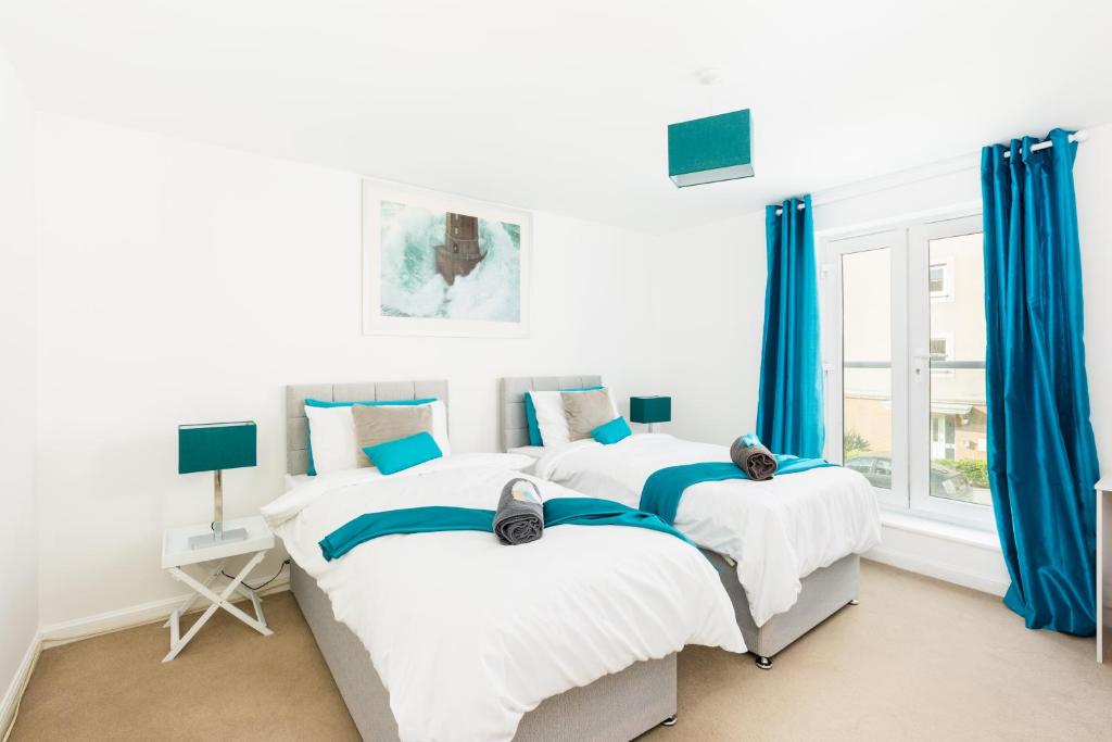 two beds in a white bedroom with blue curtains at Spacious Group House for Contractors & Families - Ensuites, Parking & Netflix by DreamyPads in Bristol