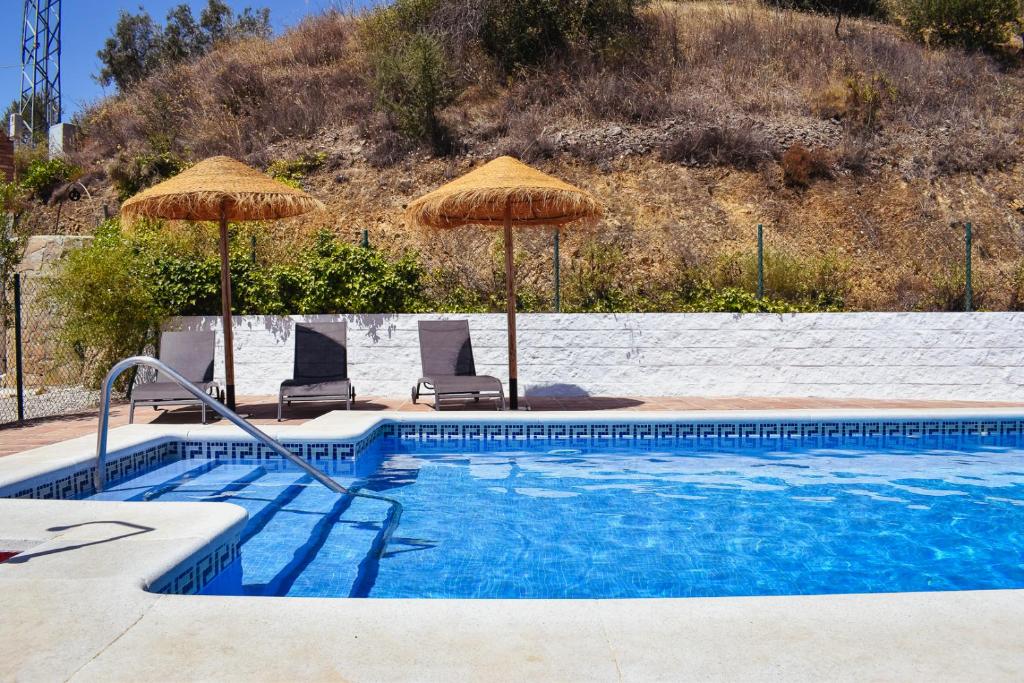 a swimming pool with two umbrellas and two chairs at Gusta la Vista in Ríogordo