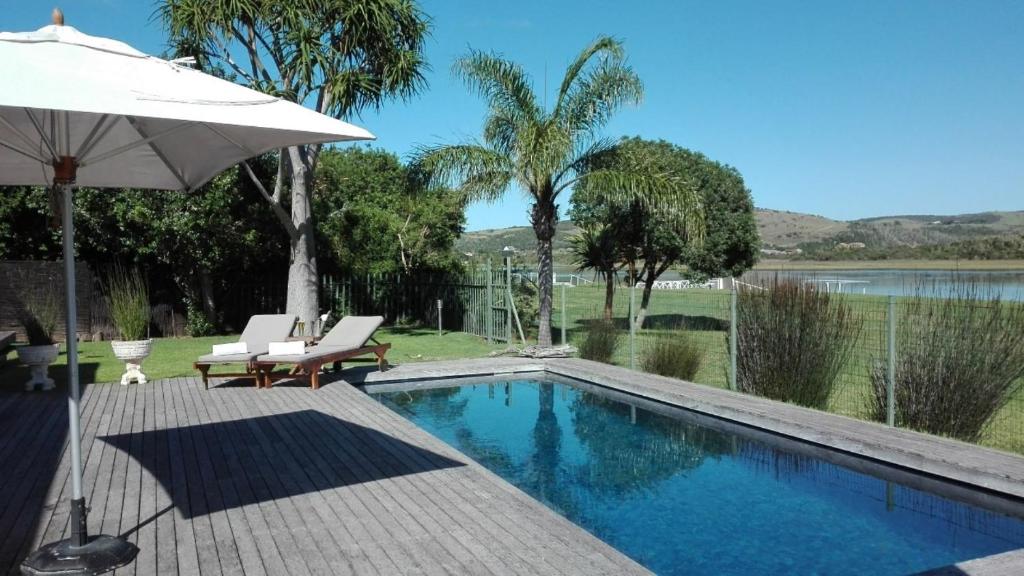 a swimming pool with an umbrella and two chairs and a table at Kowie River Guest House in Port Alfred