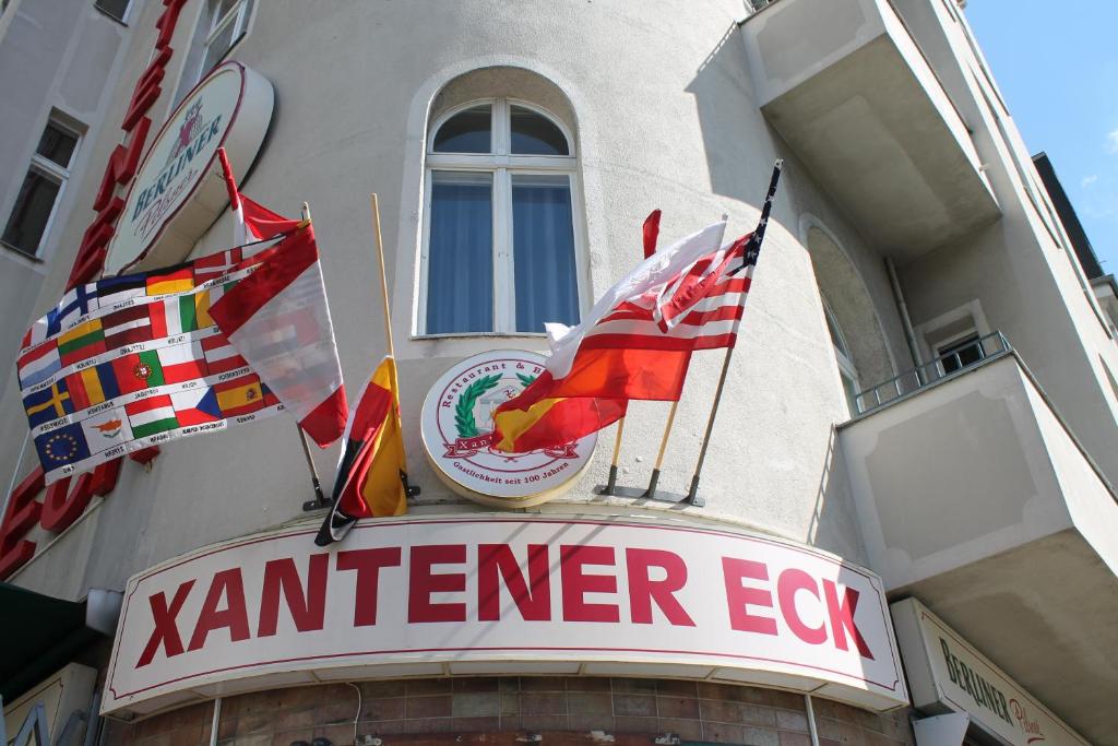 un cartel en la parte delantera de un restaurante con banderas en Hotel Pension Xantener Eck en Berlín