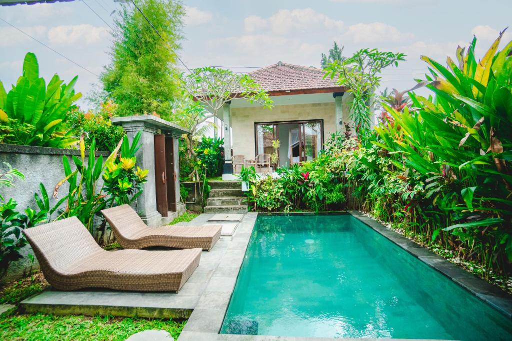 een zwembad in een tuin met twee stoelen en een huis bij Pondok Ubud Nia Cahya in Tegalalang