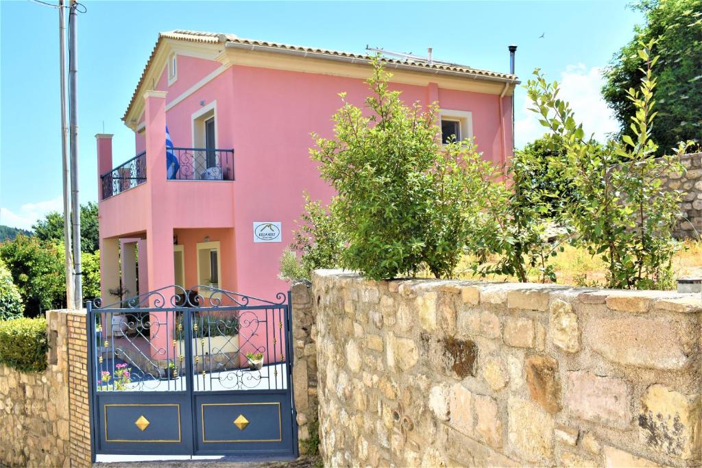 a pink house behind a stone wall with a gate at Villa Niki in Págoi